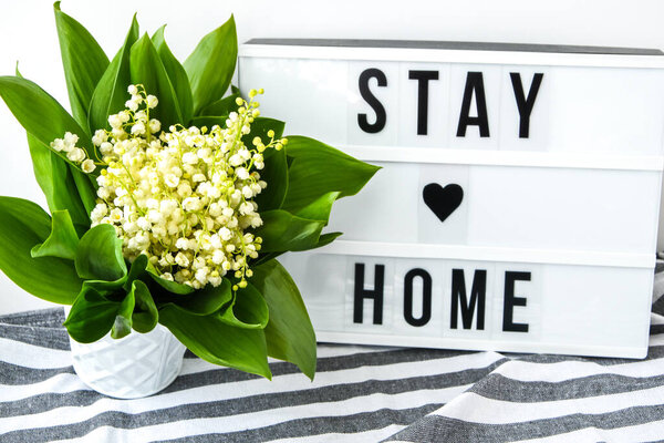 Lightbox with text STAY HOME and bouquet lilies of the valley in white bucket, spring time, quarantine, holiday background