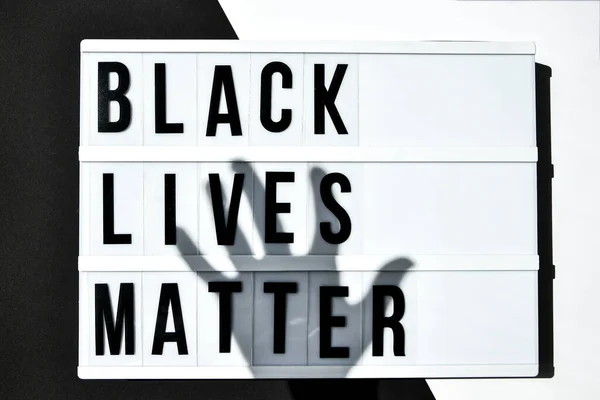 BLACK LIVES MATTER text with deep shadows of hand on a black and white background. Protest against the end of racism, anti-racism, equality. Poster on violation of human rights
