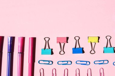 Pembe arka planda farklı ofis ya da okul malzemeleri. Metin, kalem kağıdı, ataç, etiket ve mandal için boşluk kopyala