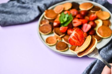 Geleneksel Krep ve Çilekli Küçük Krep Gevreği ve Karanlık Arkaplanda Nane Yaprakları ile Tabak. Moda yemekler. Küçük krepler ve çilekli çatala odaklan.