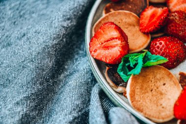 Geleneksel Krep ve Çilekli Küçük Krep Gevreği ve Karanlık Arkaplanda Nane Yaprakları ile Tabak. Moda yemekler. Mini mısır gevreği krepleri.