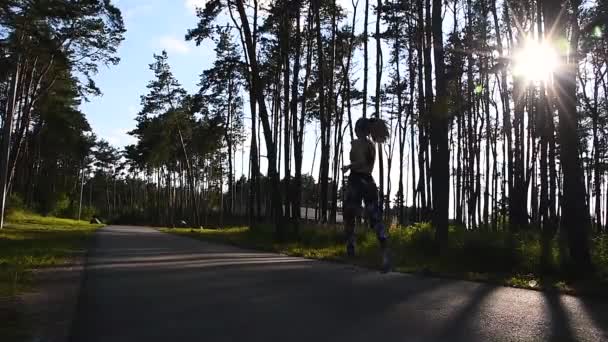 Naturaleza en forma. Chica de fitness se ejecuta en la luz de la noche. Una joven esbelta con un chándal corre en el parque a lo largo de la carretera bajo el sol. Mañana de verano fresca corriendo . — Vídeos de Stock