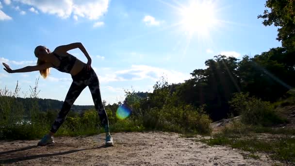 Подтянутая и здоровая женщина в спортивном костюме делает упражнения в горах при сильном солнечном свете. Тренировки, тренировки и оздоровительная концепция. Спорт на открытом воздухе. Медленное движение — стоковое видео