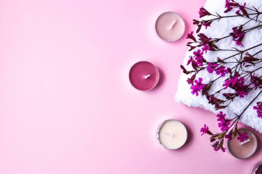 Pembe arka planda küçük pembe çiçekli beyaz pamuk havlu ve aroma mumları, kopya alanı, cilt ürünleri, spa tedavisi için doğal kozmetik ürünleri.