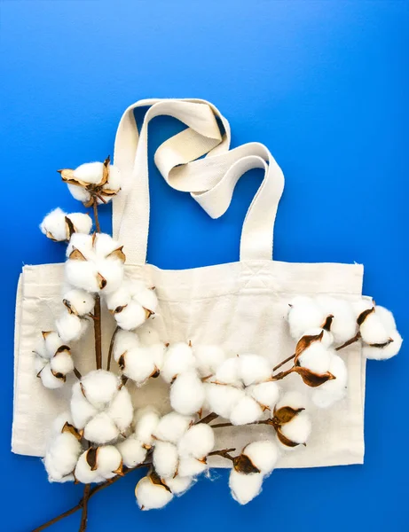 Stylish eco bags and cotton flowers on blue background, Zero waste concept. Eco-friendly shopping. Fluffy cotton flowers and Organic bags, top view