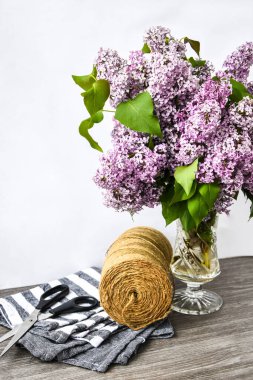 Masanın üzerinde makas, ip, fotokopi alanı ve bayram tebrikleri içeren cam vazoda leylak çiçeği.
