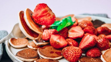 Geleneksel Krep ve Çilekli Küçük Krep Gevreği ve Karanlık Arkaplanda Nane Yaprakları ile Tabak. Moda yemekler. Küçük krepler ve çilekli çatala odaklan.