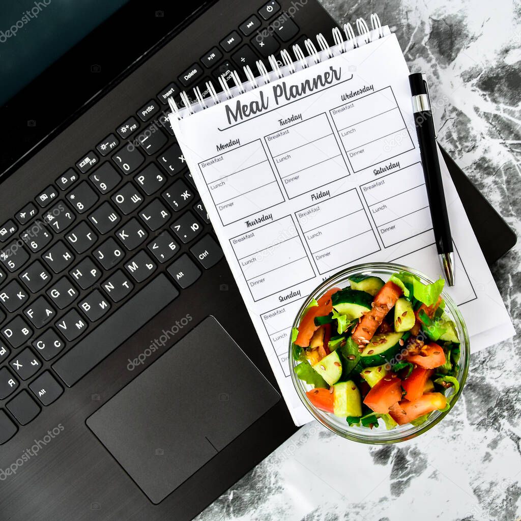 A meal plan for a week. Bowl with vegetable salad in the workplace near the computer. Lunch in the office during a break between work, Meal planner