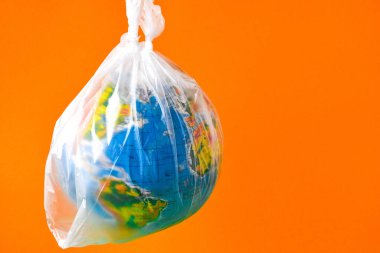 Küre şeklinde bir top plastik bir torbanın içinde. Dünyanın plastik kirliliği kavramı. Dünya Çevre Günü kavramı. Oyuncak dünya küresi beyaz plastik torba içinde. Uzayı metin için kopyala. Dünyayı Kaydet