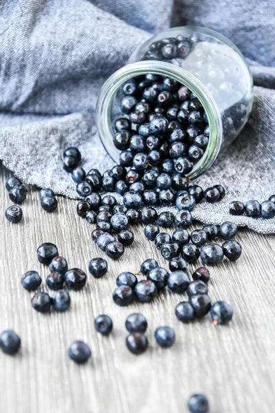 Selective focus Fresh Blueberries spilled from glass jar on wooden background. Juicy wild forest berries, bilberries. Healthy eating or nutrition.