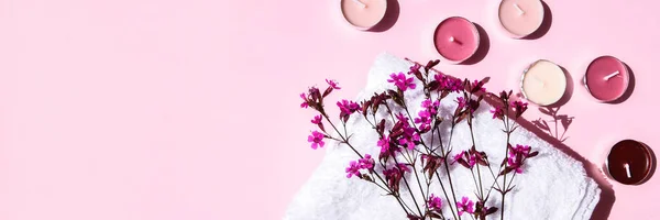 ピンクの背景に小さなピンクの花や香りのキャンドルと白い綿のタオル コピースペース スキンケア製品 ホームスパの治療のための天然化粧品 — ストック写真