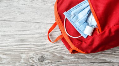 Kırmızı okul çantası, tıbbi maske ve ahşap masada antiseptik. Okul konseptine geri dönelim. Okul karantina konsepti. Metin için alanı kopyala