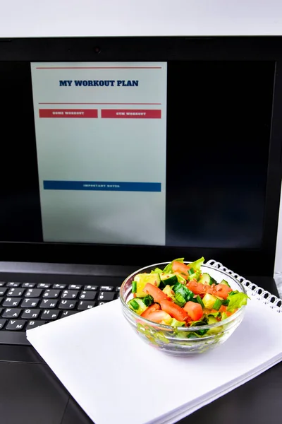 Exercise plan for a week. Bowl with vegetable salad in the workplace near the computer. Lunch in the office during a break between work, Workout planner