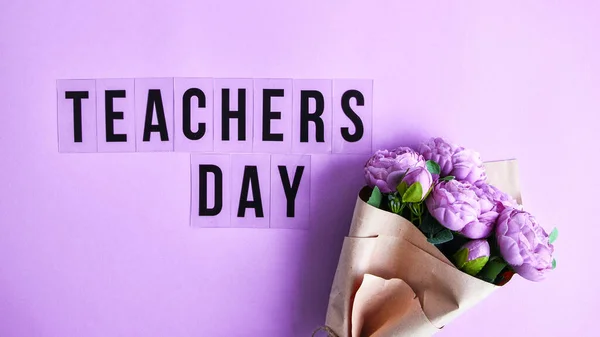 Text TEACHERS DAY on lilac background with bouquet of flowers peonies. School holidays. Back to school