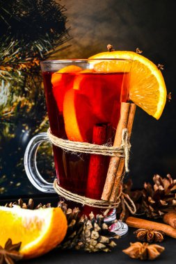 Sıcak şarap, arka planda baharatlar olan sıcak noel içeceği. Portakal dilimleri, tarçın çubukları, noel konileri, parlak bokeh. Tatil atmosferi, taşra tarzı. Tebrik kartları oluşturma fikri