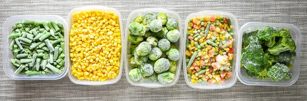 Plastic containers with frozen vegetables on grey background, top view, Different frozen vegetables on table, trendy food, corn brussels sprouts mixed green beans. Stocking up vegetables for winter storage