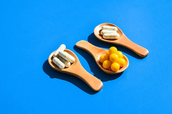 Tabletták Kapszulák Fából Készült Kanalakon Kék Alapon Kemény Fény Árnyékok — Stock Fotó