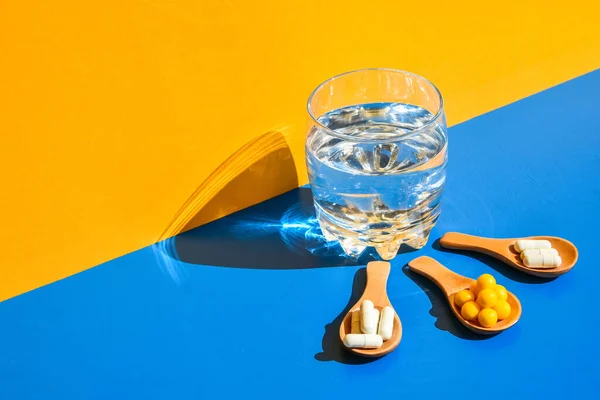 Vaso Agua Pastillas Sobre Cuchara Madera Sobre Fondo Azul Amarillo — Foto de Stock