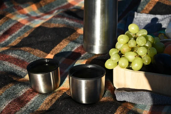 Autumn picnic tea thermos with grapes and peaches. Fruits and Tea on blanket. Outdoor lunch. Picnic with tea in a thermos. A convenient blanket to relax in the woods and Breakfast.