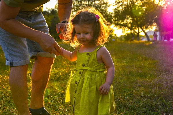 Schattig klein meisje neemt handen met haar vader. Lopen met kinderen concept imago. Klein meisje die haar ouders hand in hand houdt. Glimlachende baby in jurk. — Stockfoto