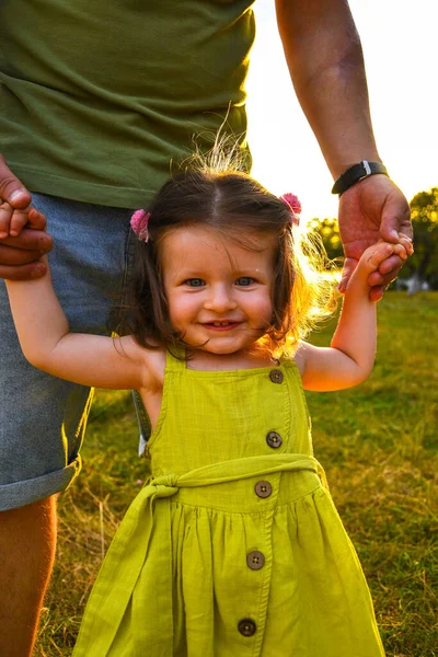 Schattig klein meisje neemt handen met haar vader. Lopen met kinderen concept imago. Klein meisje die haar ouders hand in hand houdt. Glimlachende baby in jurk. — Stockfoto