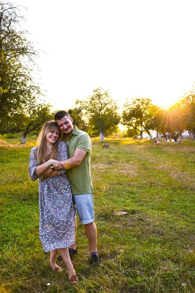 Giovane mamma papà di famiglia che cammina la sera in un parco con alberi alla luce del tramonto. Un paio di abbracci. Felice giovane coppia godendo all'aperto durante il tramonto — Foto Stock