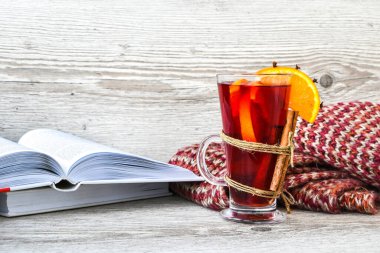 Sıcak şarap, ahşap arka planda baharatlar olan sıcak noel içeceği. Portakal dilimi, tarçın çubukları, kitaplar ve kazak. Noel sabahı. Tatil atmosferi, taşra tarzı. Tebrik kartı yapma fikri. Sonbahar içeceği