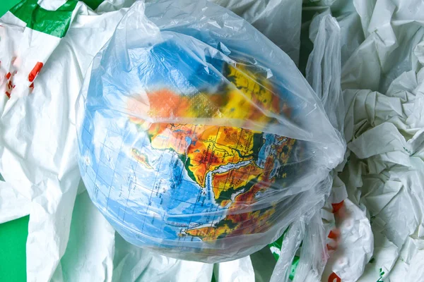 globe is in a plastic bagon trash. concept of plastic pollution of the earth. World Environment Day concept.Toy world globe in white plastic bag. Copy space for text. Save Earth