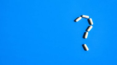 Mavi arka planda beyaz haplar, haplar ve kapsüllerden oluşan soru işareti. İlaç endüstrisi ve reçeteli asgari konsept. Uzayı kopyala Vitaminler prebiyotikler ve probiyotikler