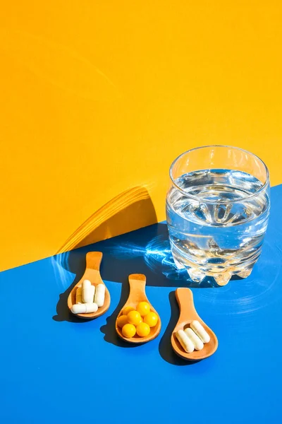 Vaso Agua Pastillas Sobre Cuchara Madera Sobre Fondo Azul Amarillo — Foto de Stock