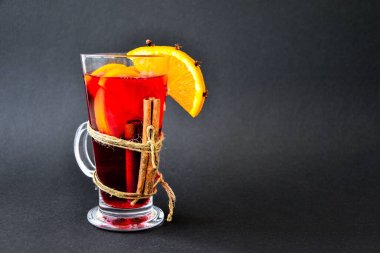 Baharatlı Noel şarabı ve koyu siyah arka planda portakal. Seçici odaklanma. Anason yıldızları ve tarçın çubukları. Noel konileri. Metin için alanı kopyala