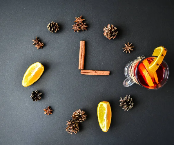 A clock in the form of spice for mulled wine on black background. Cinnamon sticks, anise stars, pine cones, slice of orange. Concept, creative work. Top view. Holiday atmosphere, Rustic style. The idea for creating greeting cards