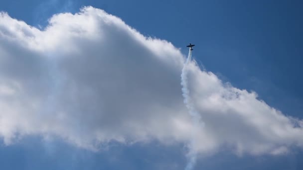 黒い飛行機は空を飛んで煙を放出する。航空機は航空ショーでループを実行します。輸送装置は異常な操縦及びトリックを作る。飛行機は雲の中を飛んでいる. — ストック動画
