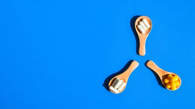 Haplar ve kapsüller mavi arka planda tahta kaşıklarda. Sert ışık ve gölgeler. Uzayı kopyala Vitaminler prebiyotik probiyotikleri. İlaç dozunda. Sağlık hizmetleri.