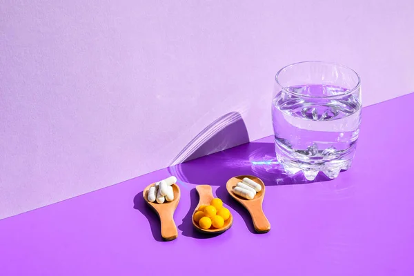 Glas Wasser Und Pillen Auf Holzlöffel Auf Violettem Hintergrund Mit — Stockfoto