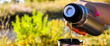 Gezgin sonbaharda düşen ormanda termostan fincana sıcak çay döker. Yaz sonbahar pikniği. Boşluğu kopyala