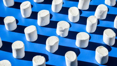 Birçok beyaz marşmelov silindirik şekil mavi arka planda yatar. Sağlıksız abur cubur kalıpları. Şekerlemeler