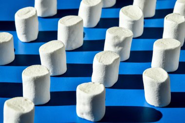 Birçok beyaz marşmelov silindirik şekil mavi arka planda yatar. Sağlıksız abur cubur kalıpları. Şekerlemeler