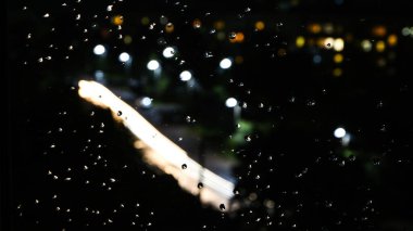 Pencere camındaki yağmur damlaları ve gece lambaları arka planda. Bulanık ışıklar. Soyut yağmur arkaplanı