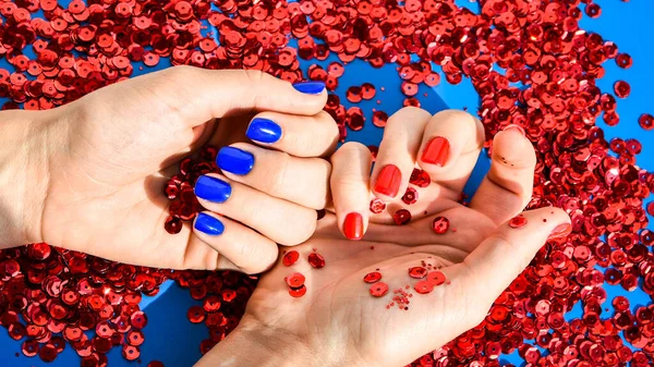 Hand with blue and red nails on red bright background. Female manicure. glamorous beautiful manicure. Winter or autumn manicure in blue and red. Fashionable Nail Gel Polish Color
