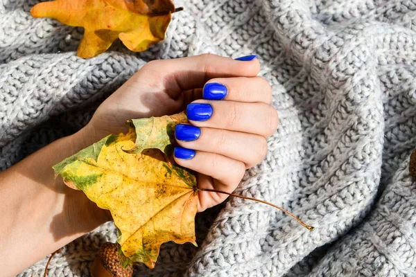 Hand with blue nails on sweater autumn cozy background. Female manicure. glamorous beautiful manicure. Winter or autumn manicure in blue. Fashionable Nail Gel Polish Color