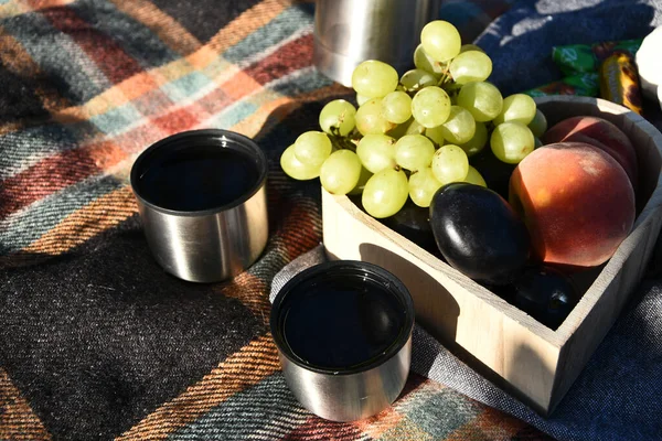 Autumn picnic tea thermos with grapes and peaches. Fruits and Tea on blanket. Outdoor lunch. Picnic with tea in a thermos. A convenient blanket to relax in the woods and Breakfast.