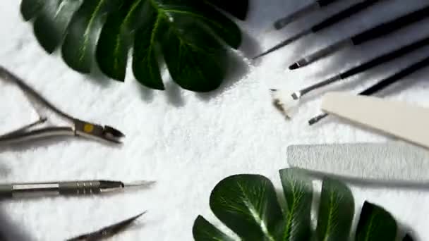 Manicure - gereedschappen draaien voor het maken, gel poetsmiddelen, allemaal voor de behandeling van nagels, het concept van schoonheid, zorg met groene bladeren op witte handdoek achtergrond. — Stockvideo