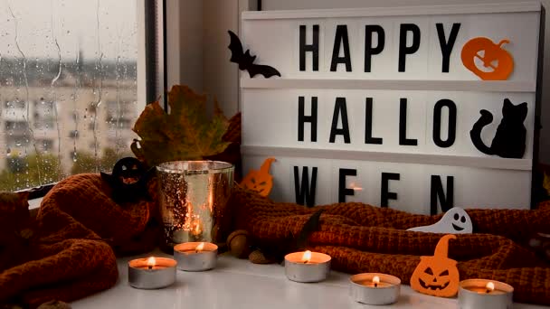 Herfst Allerheiligen. Halloween decoraties op vensterbank met brandende kaarsen. Regenachtige dagen buiten. De regen klopt op het glas. — Stockvideo