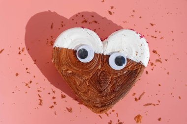 Kalp şeklinde beyaz çikolatalı kruvasan ve pembe arka planda fotokopi alanı olan komik gözler. 1 Nisan şakası fikri Puff pastası yeni moda tatlı pastanesi. Kremalı hamur deneyi 