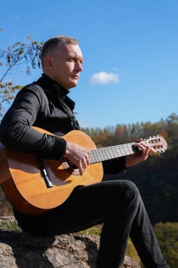 Sonbahar ormanında dışarıda gitar çalan sarışın bir adam. Ses terapisi, akıl sağlığı ve sağlık ayinleri kavramı. Sakinlik sükuneti ses duyusal uygulamaları. Aura tarım enerjisi bütünsel