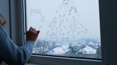 Süveter boyalı camlı, beyaz kalemli, yaratıcı, hevesli, tanınmaz bir kadın. Büyük açık pencerede Noel ağacı süslemesi. Dışarıda karlı bir kış var. Tatil hazırlığı 