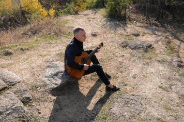 Sonbahar ormanında dışarıda gitar çalan sarışın bir adam. Ses terapisi, akıl sağlığı ve sağlık ayinleri kavramı. Sakinlik sükuneti ses duyusal uygulamaları. Aura tarım enerjisi bütünsel