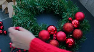 Şenlikli kırmızı süslemelerden elde yapılmış el yapımı Noel çelengi kullanan el sanatları ustası. Tatil hazırlığı, yaratıcı dekorasyon ustası sınıfı. Etkin faaliyetler sürdürülebilir sorumluluk