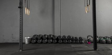 Dambıllar de varios pesos en muro de crossfit con aros de gimnasia a los lados